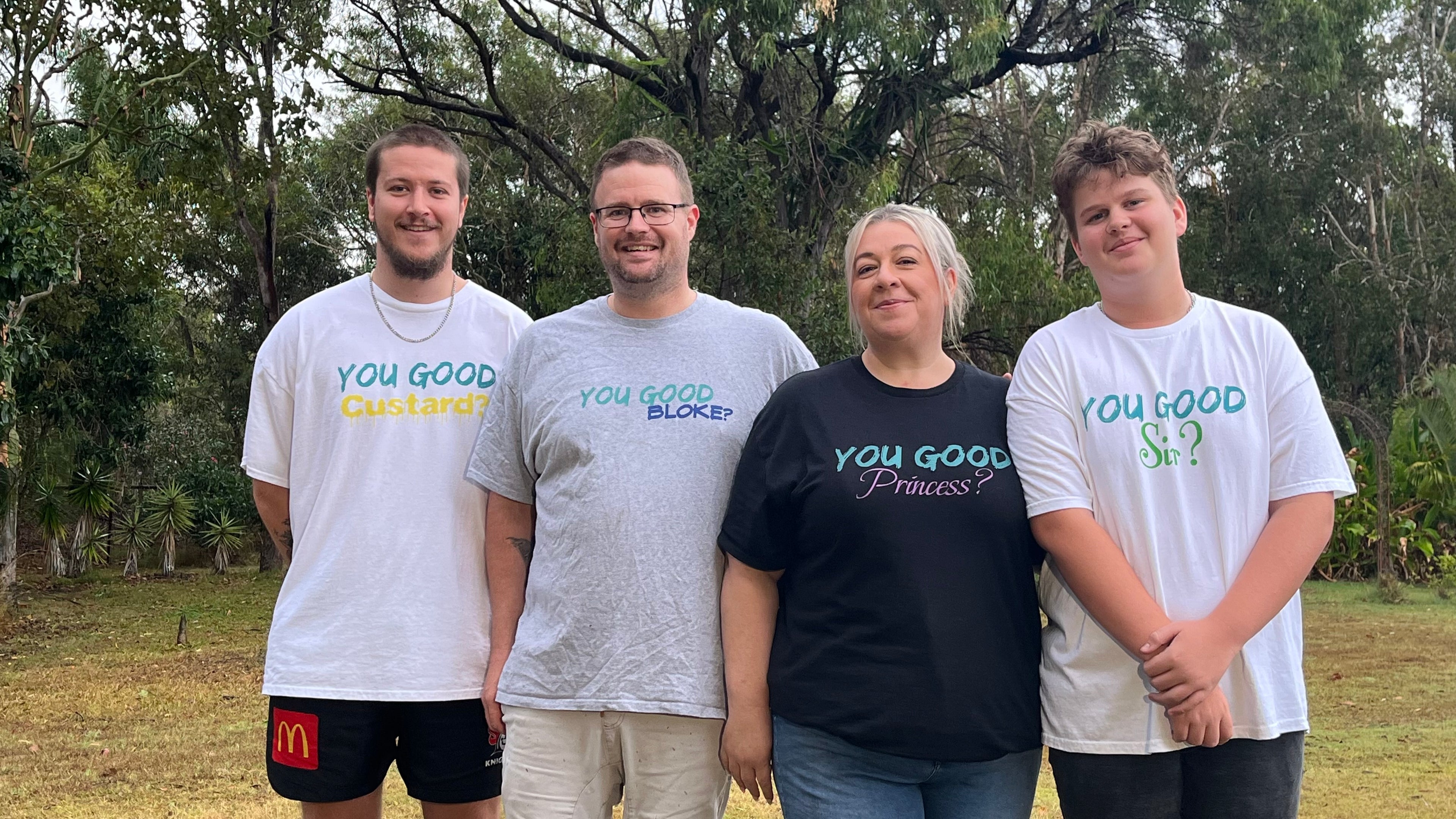 Four people wearing 'You Good' branded shirts outdoors with trees in the background
